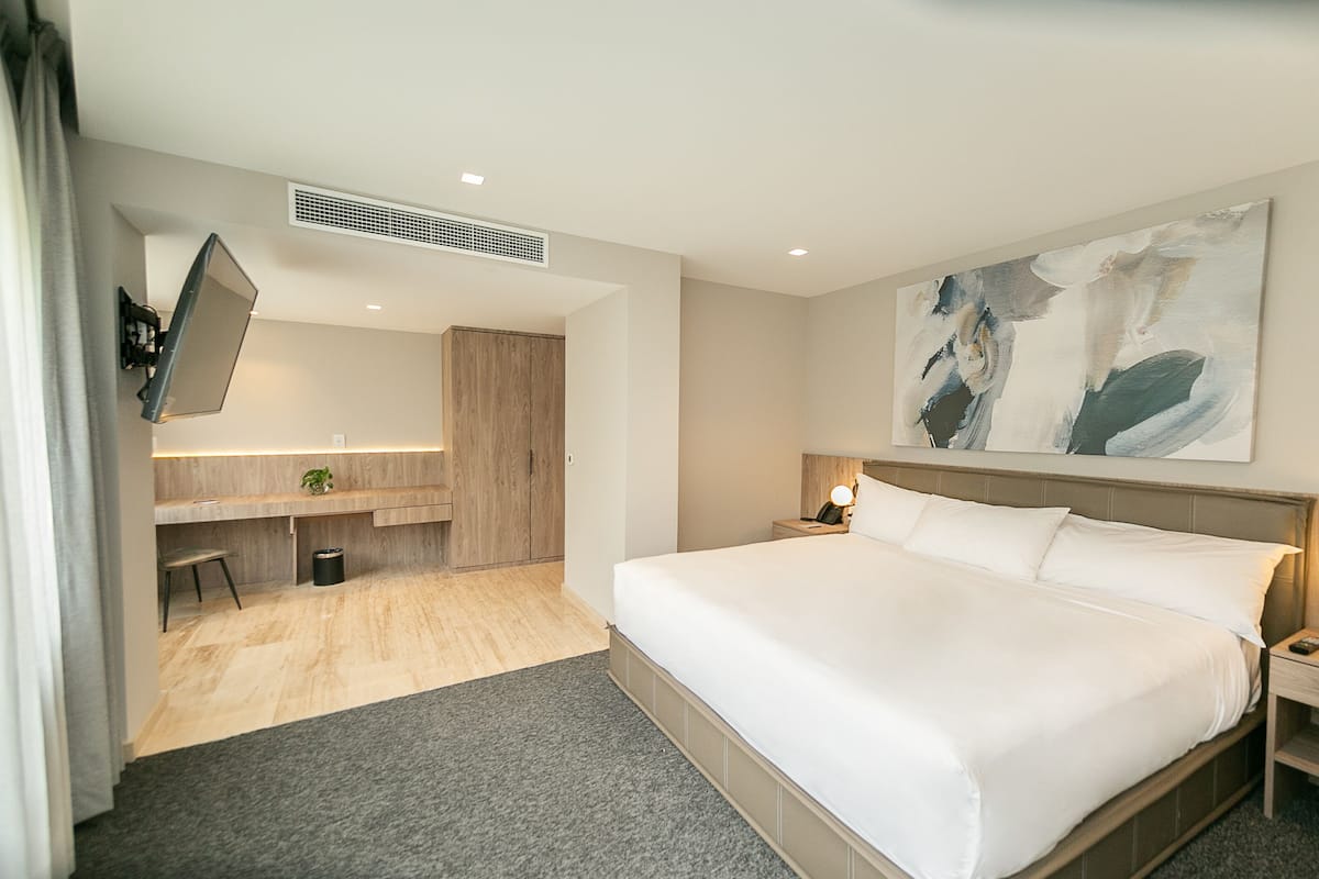A hotel room with a large bed, a desk with a chair, a small table, and a painting on the wall.