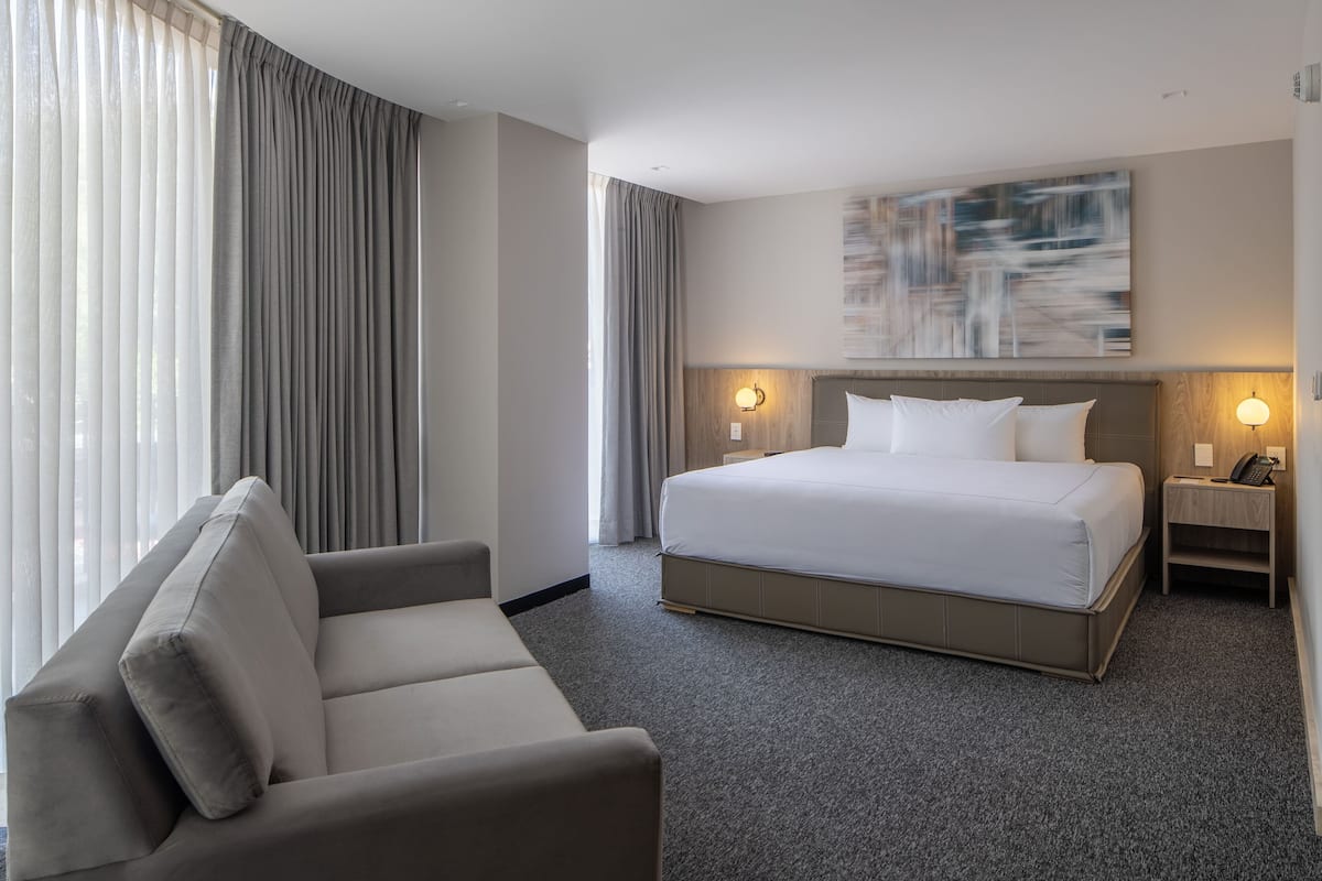 A hotel room with a large bed, a sofa, two bedside tables with lamps, and a large abstract painting on the wall.