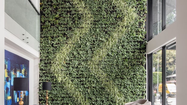Un vestíbulo moderno con un jardín vertical verde, un sofá de cuero negro, una mesa de centro de madera y una escultura de madera única.