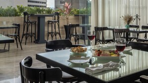 Un área de comedor en la azotea con una mesa de vidrio, sillas y vistas a edificios y vegetación.