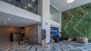 Un vestíbulo moderno con mostrador de recepción, zona de estar y una pared verde con plantas.