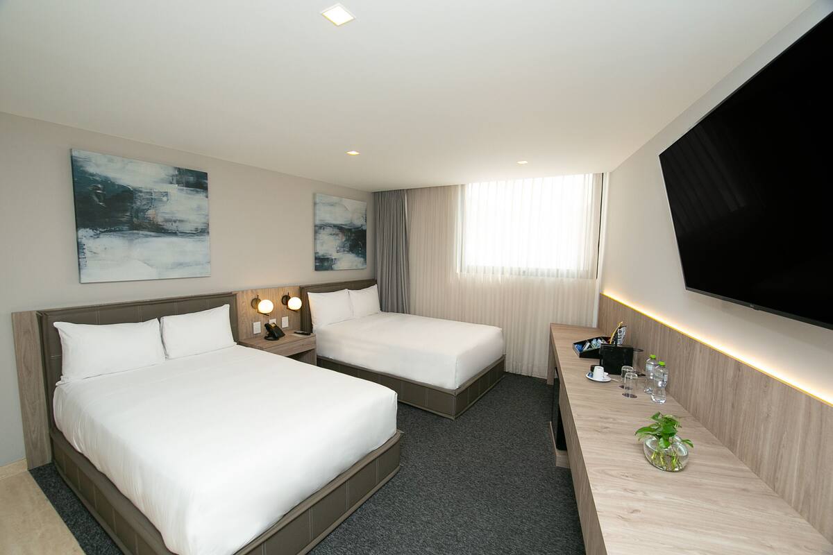 A hotel room with two beds, a desk with a flat-screen TV, and artwork on the walls.