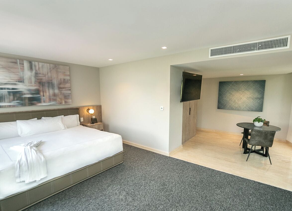 A hotel room with a bed, bedside table, lamp, and a small dining area with a table and chairs.