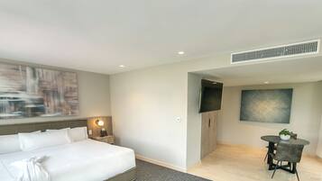 A hotel room with a bed, bedside table, lamp, and a small dining area with a table and chairs.