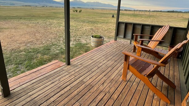 Eine Holzdauerdecke mit Adirondack-Stühlen mit Blick auf ein Wiesenfeld und Berge.