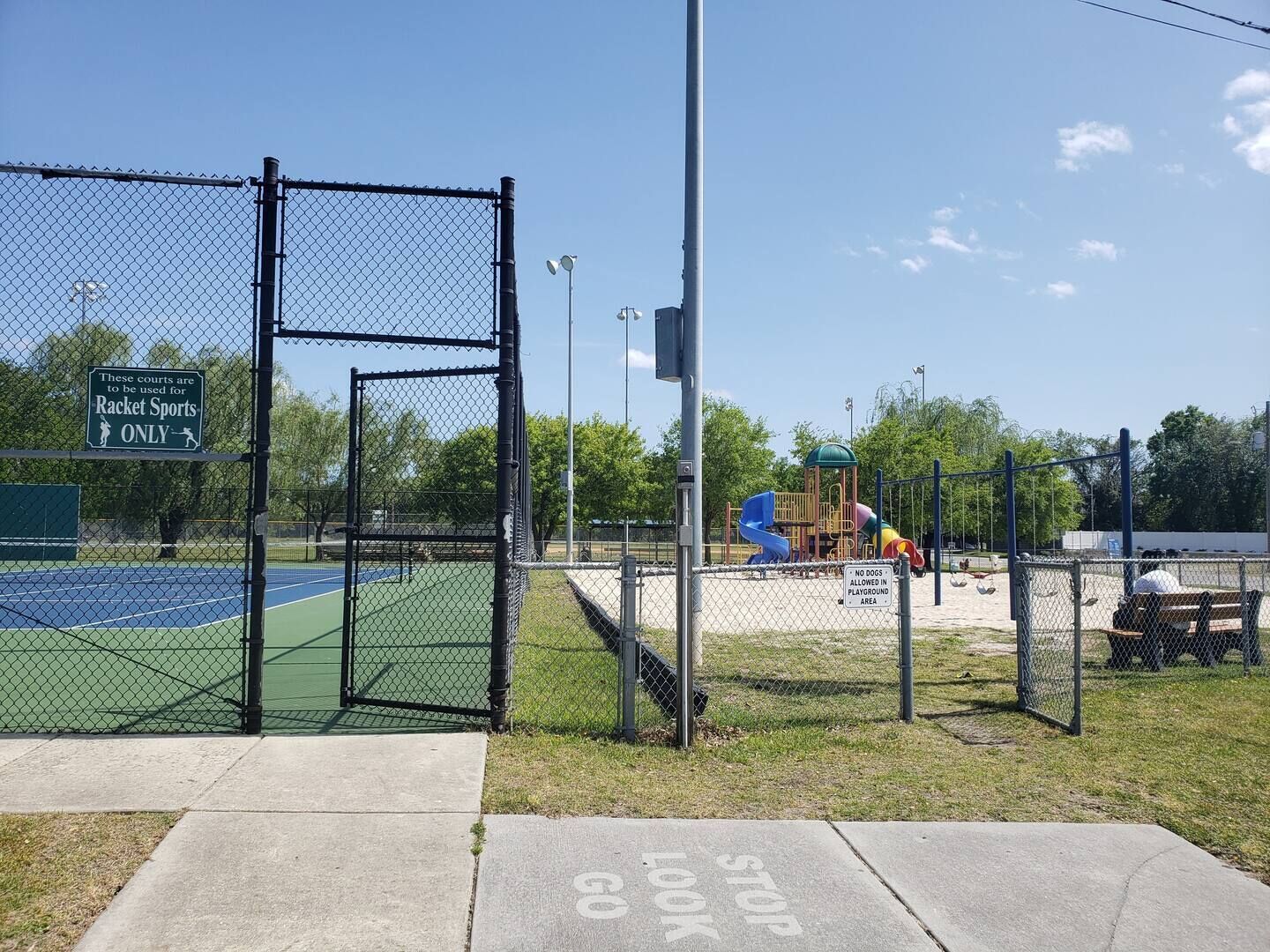 Un terrain de tennis délimité par une clôture, avec un panneau indiquant qu’il est réservé aux sports de raquette.