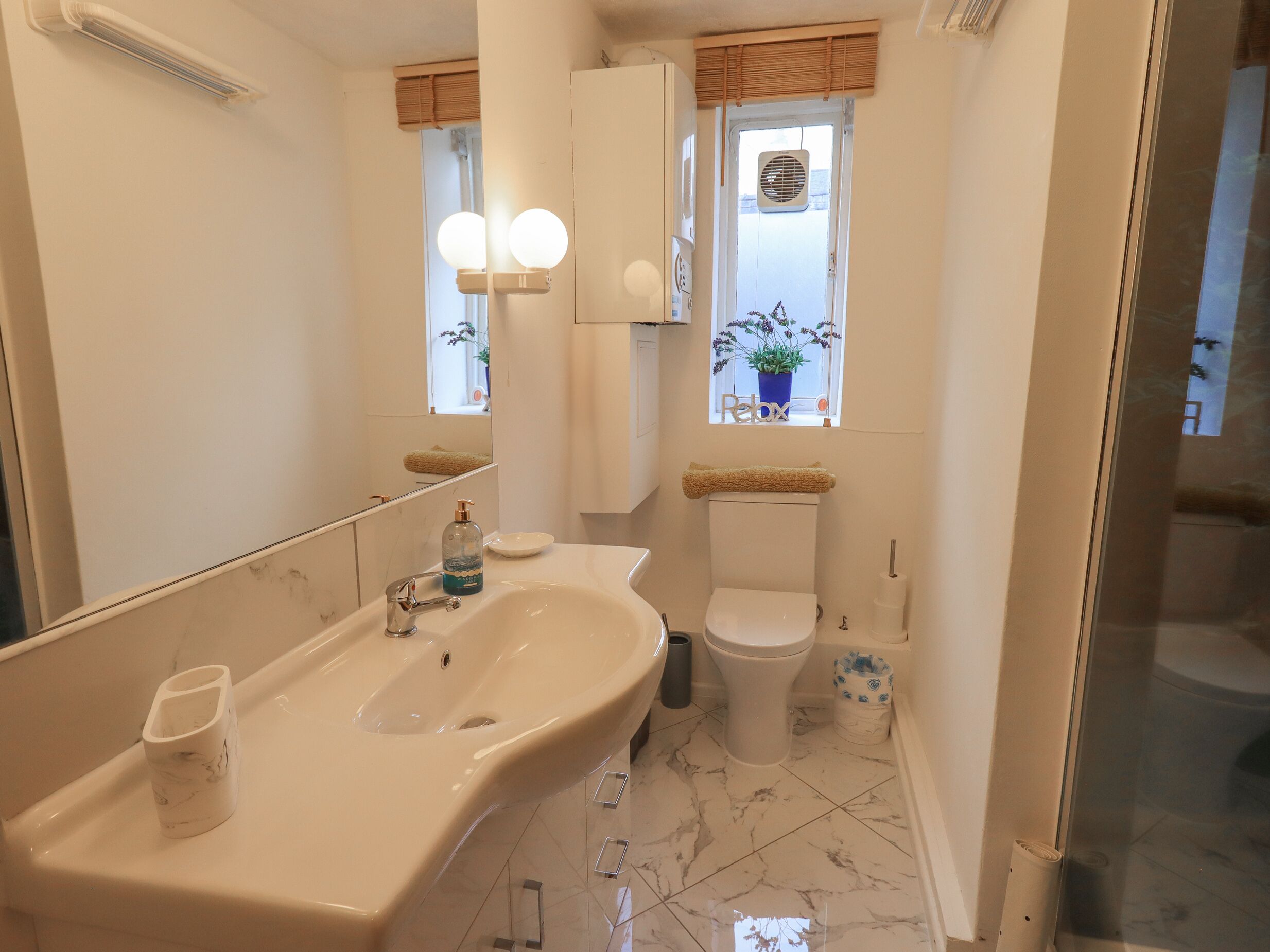 A bathroom with a large sink, toilet, and a window with a plant.