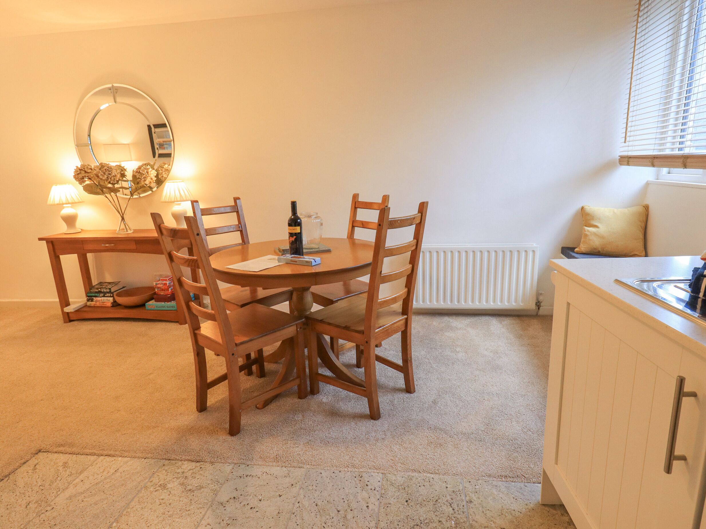 A cozy dining area with a round table, wooden chairs, a mirror, and a small side table with a lamp and decorative items.
