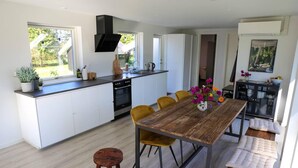 A modern kitchen with white cabinets, a wooden dining table, and a built-in oven. - The Comfort of This Cottage Merges With Nature (Holbaek)