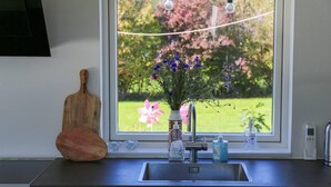 A kitchen with a window, a wooden cutting board, a vase with flowers, and a faucet. - The Comfort of This Cottage Merges With Nature (Holbaek)