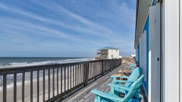 A wooden deck with chairs, a view of the ocean, and a building with a blue roof.