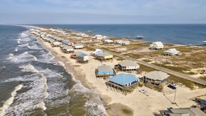 An aerial view of a coastal area with beach houses, a road, and the ocean.