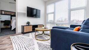 A modern living room with a blue sofa, a round wooden coffee table, and a TV mounted on the wall. - Yugo Guest Suites (Urbana)