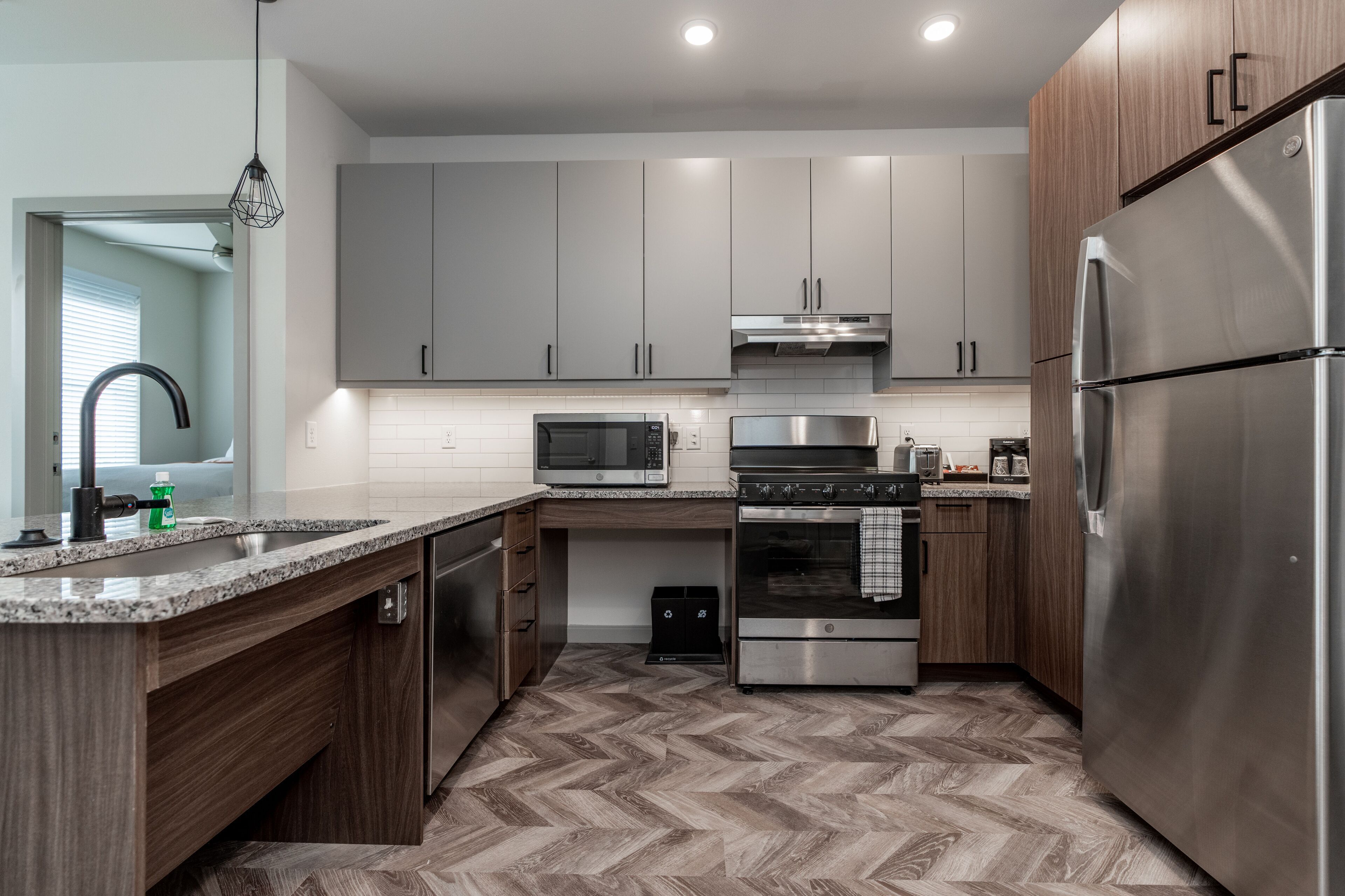 Una cocina moderna con armarios grises, electrodomésticos de acero inoxidable y un suelo con estampado en espiga.
