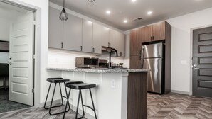A modern kitchen with a central island, stainless steel appliances, and a herringbone-patterned floor. - Yugo Guest Suites (Urbana)