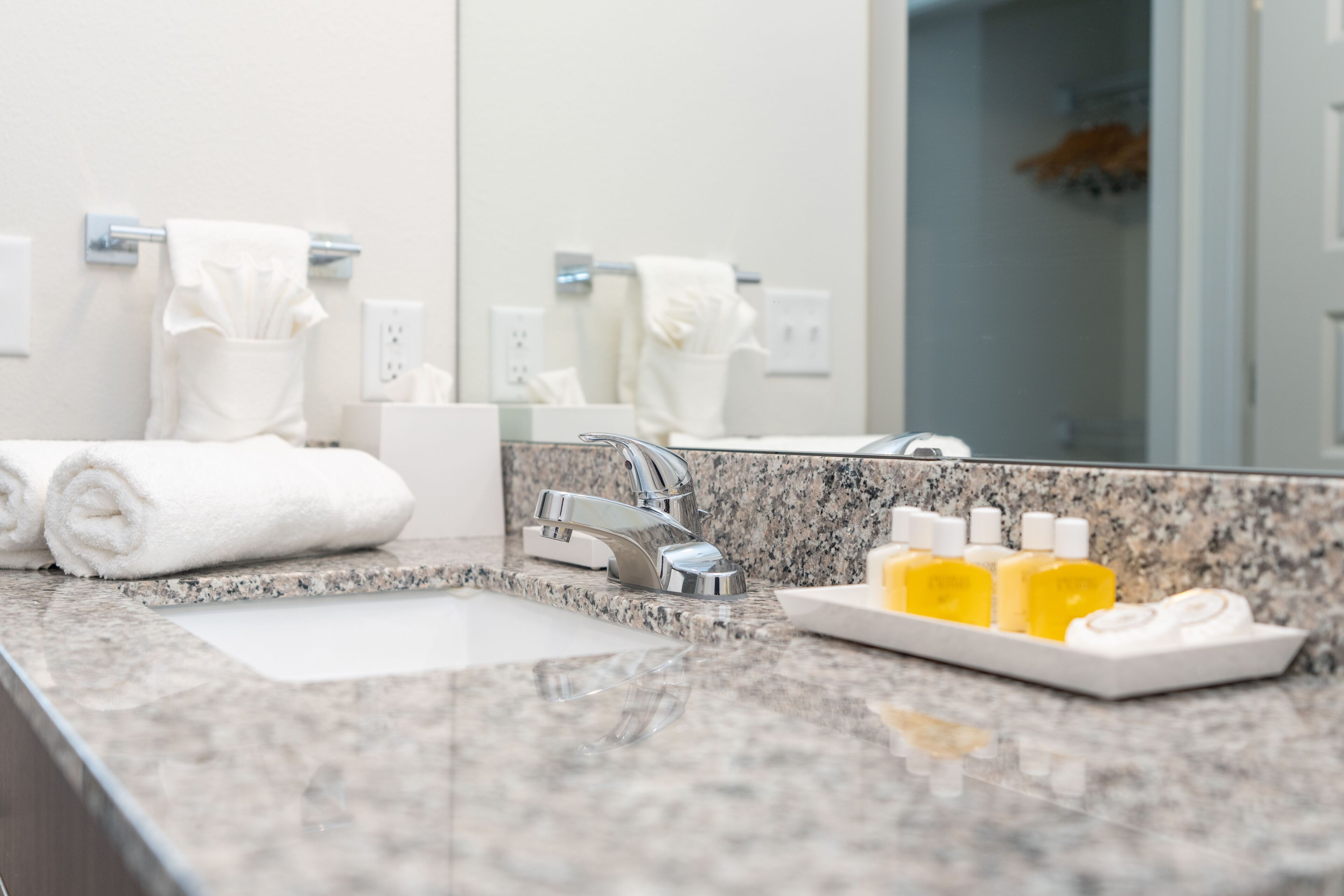 A bathroom with a granite countertop, a sink, a mirror, and a towel rack.
