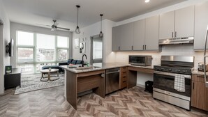 A modern kitchen with a herringbone floor pattern, stainless steel appliances, and a built-in oven. - Yugo Guest Suites (Urbana)