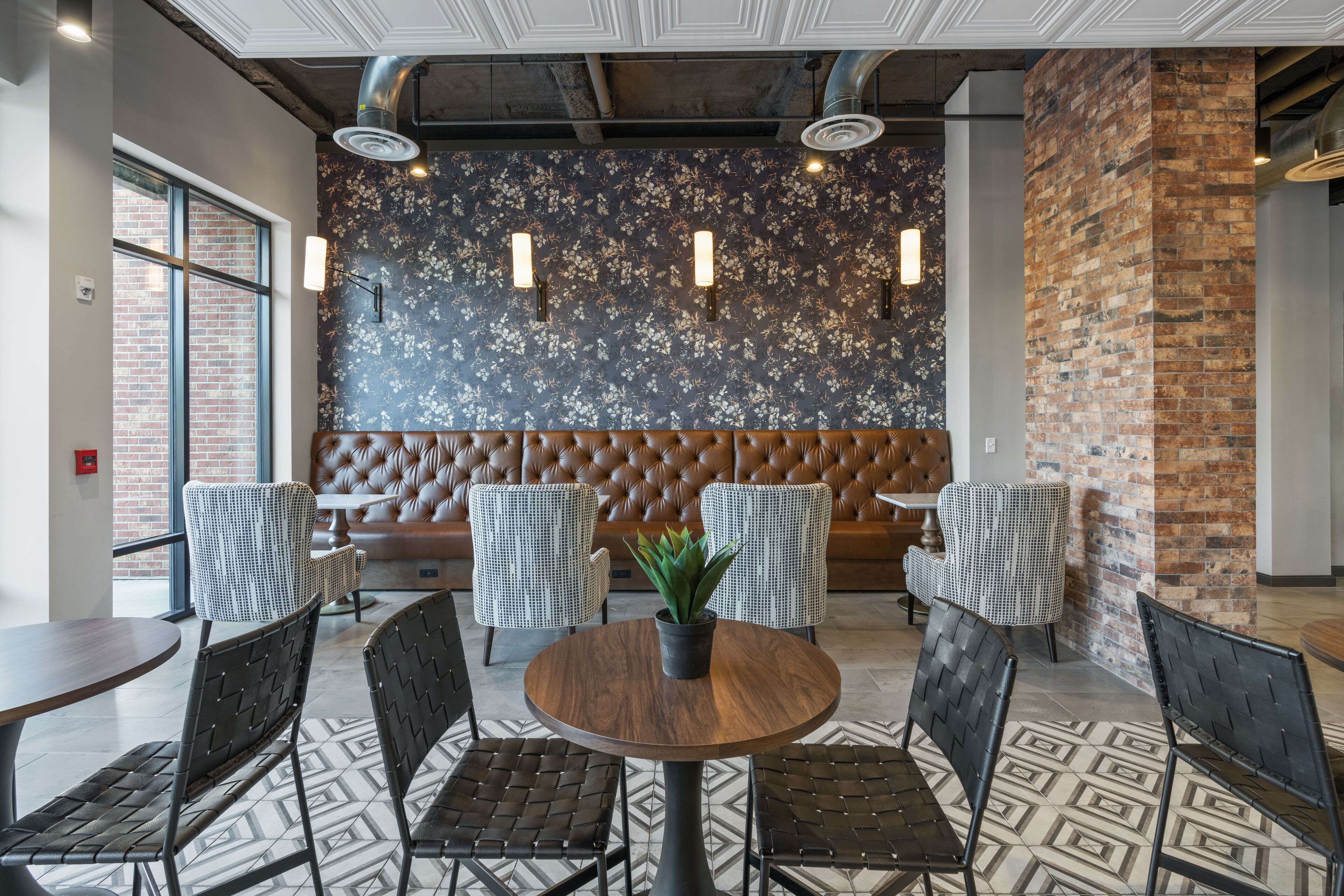 A modern interior with a round wooden table surrounded by black chairs, a brown cushioned bench, and a patterned floor.