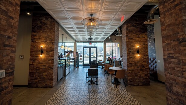 A spacious lobby with a patterned floor, brick walls, and a central chandelier. - Yugo Guest Suites (Urbana)