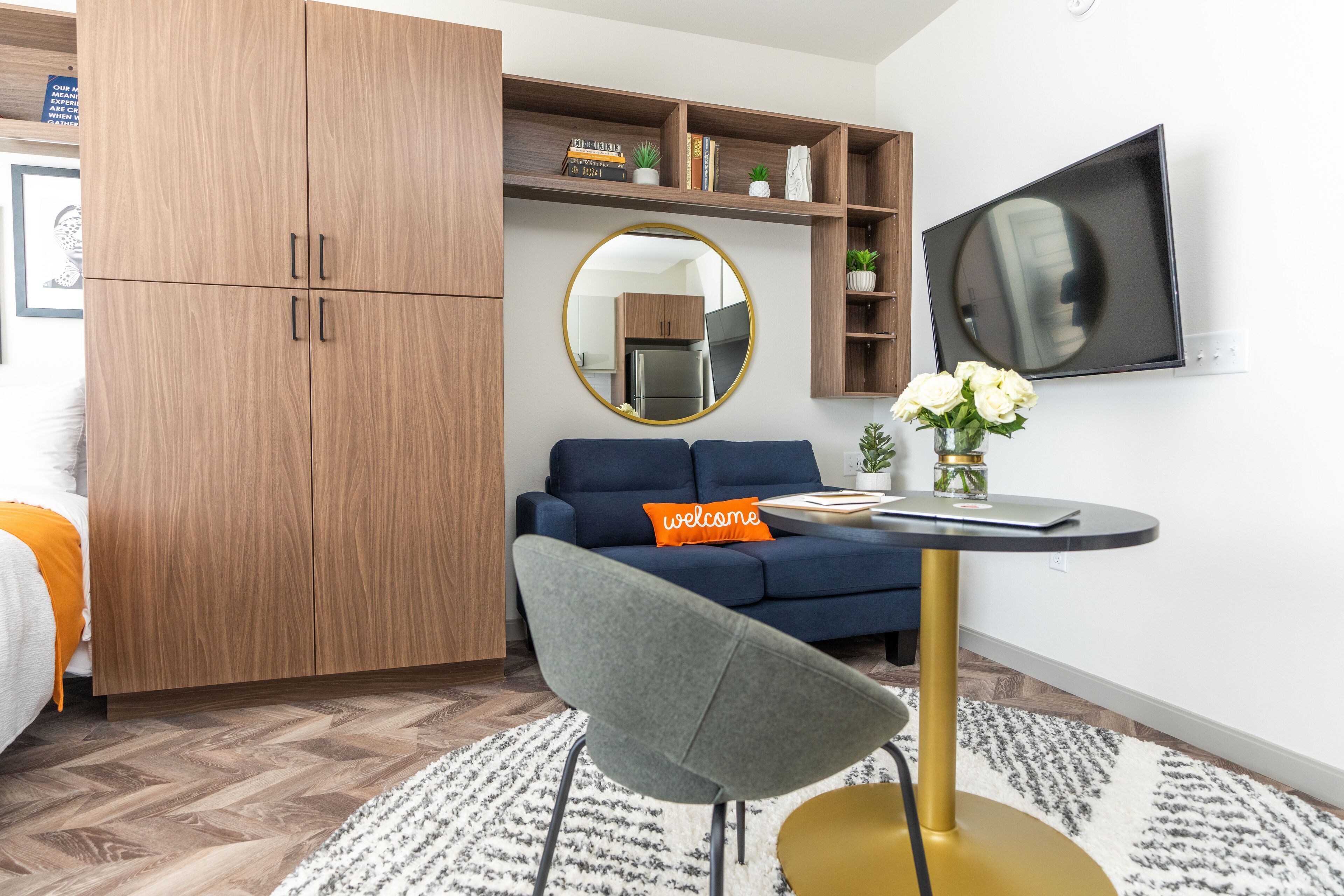 A modern living room with a sofa, a round mirror, a TV, and a bookshelf.