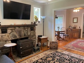 A living room with a stone fireplace, a television mounted on the wall, a dining area with a table and chairs, and a patterned rug on the floor.