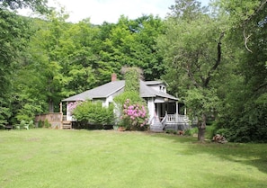 A house with a porch, surrounded by a well-maintained lawn and dense trees.