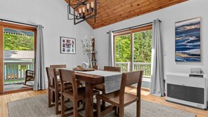 A dining area with a wooden table and chairs, a chandelier, and large windows with curtains.