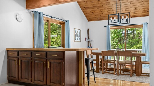 A kitchen with wooden cabinets, a dining table with chairs, and a view of greenery outside.