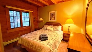 Ein Schlafzimmer einer Holzhütte mit einem Bett, einem Nachttisch, einer Lampe und einem Fenster.