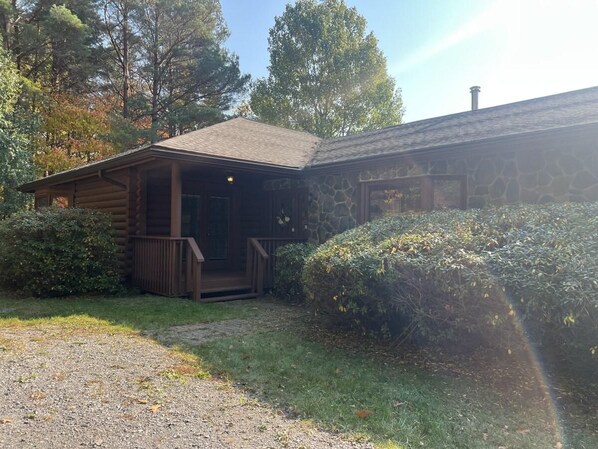 Eine Blockhütte mit Veranda, umgeben von einem Schotterweg und dichter Strauchsvegetation.