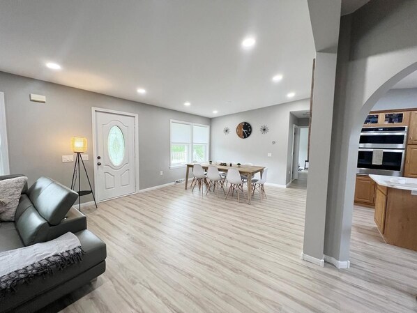A spacious living area with a dining table and chairs, a sofa, a lamp, and a kitchen area with cabinets and appliances. - Escape to Serenity: 18-Acre Catskill Retreat (Margaretville)