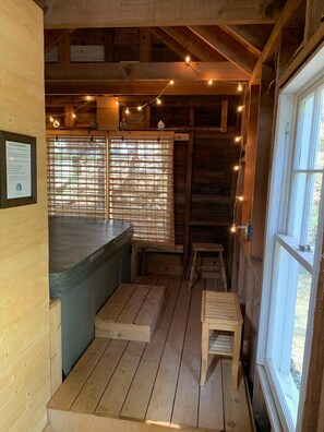 L’intérieur d’une cabane en bois comprend un coin cuisine, un plancher en bois, un banc et une fenêtre avec des stores.