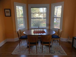 Un comedor con una mesa redonda, cuatro sillas y un tapete. Hay tres ventanas con vistas a árboles.