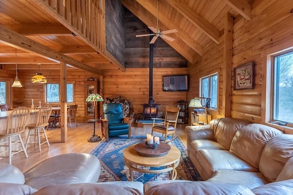 A cozy cabin interior with a dining area, a fireplace, leather seating, and a ceiling fan.
