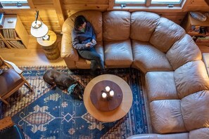 A cozy room with a curved leather sofa, a small wooden table with candles, a patterned rug, and a dog.