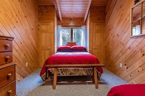Quarto pequeno com paredes de madeira e uma cama com roupa de cama vermelha.