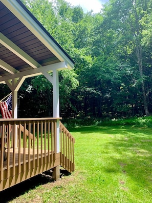 A wooden deck with a railing, a flag, and a covered area with a roof. - Cabin in the Heart of the Catskills (Arkville)