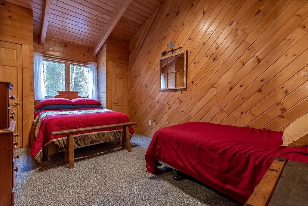 A wooden cabin bedroom with two beds, a window, and a wooden ceiling.