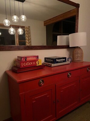 A red dresser with a mirror above it, reflecting a window and a lamp.