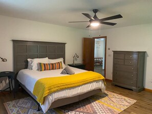 A bedroom with a bed, a nightstand, a dresser, a ceiling fan, and a door leading to another room. - Cozy, Spacious Cabin with Kid-Friendly Amenities (Roxbury)