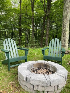 Two Adirondack chairs and a stone fire pit in a forested area. - Cozy, Spacious Cabin with Kid-Friendly Amenities (Roxbury)