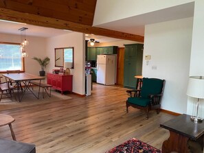 A spacious living area with a wooden floor, a dining table, a red cabinet, and a green chair. - Cozy, Spacious Cabin with Kid-Friendly Amenities (Roxbury)