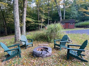 A campsite with a fire pit and four Adirondack chairs.