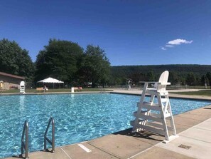 A swimming pool with a ladder and a lifeguard chair, surrounded by trees and a clear sky.