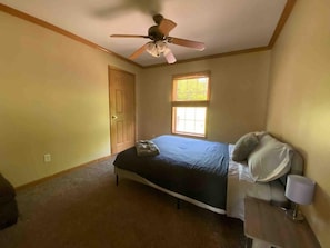 A bedroom with a bed, a ceiling fan, a window, and a door.