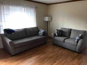 A living room with two grey sofas, a floor lamp, and a window with sheer curtains.