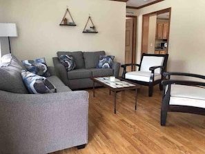 A living room with a grey sofa, a coffee table, and a chair. There are two wall decorations above the sofa.