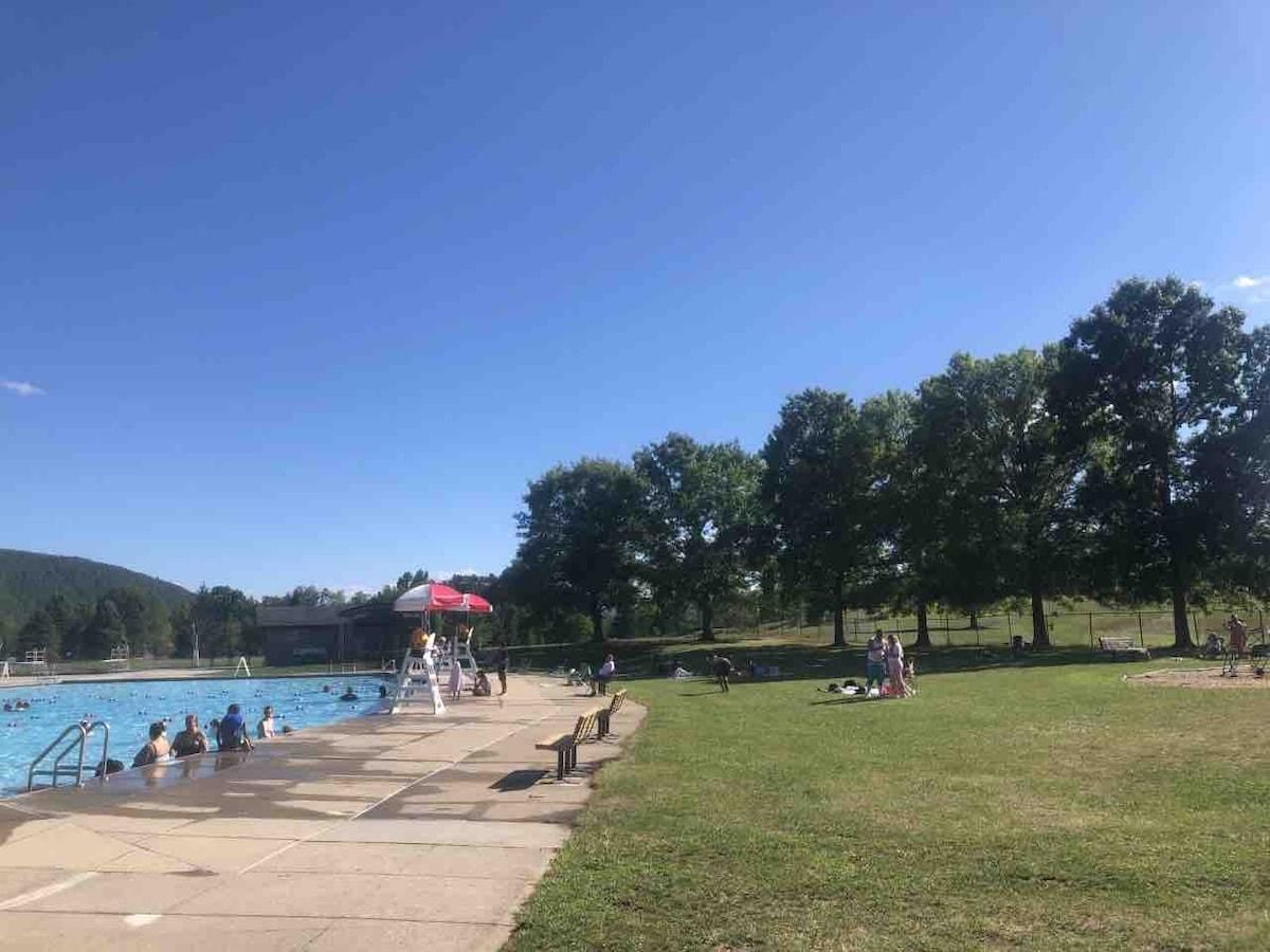 A pool area with a red umbrella, a grassy area, and trees in the background.