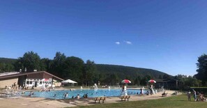 A swimming pool area with a building in the background, surrounded by trees and hills.