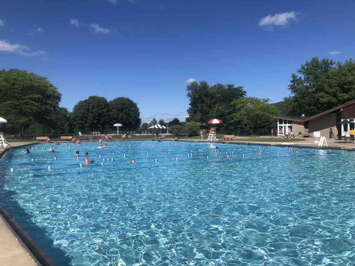 Uma piscina com água azul cristalina, rodeada por árvores e um edifício com telhado vermelho.